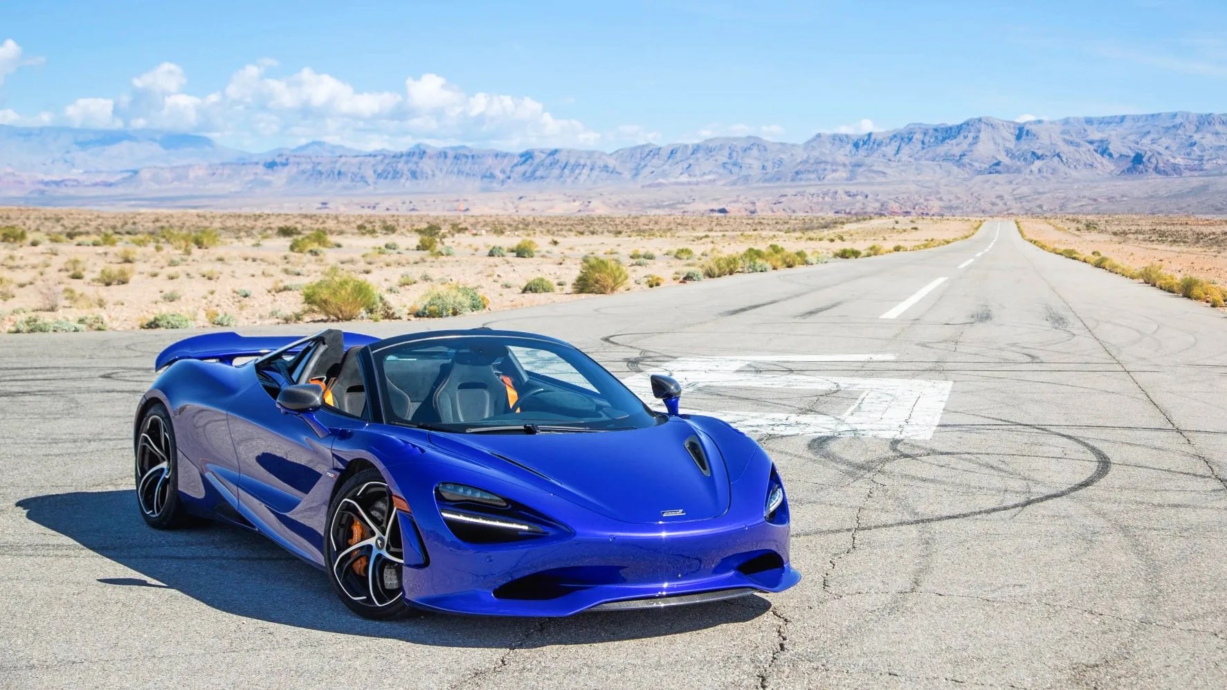 a purple blue mclaren 750s spider parked on a runway with mountains in the background